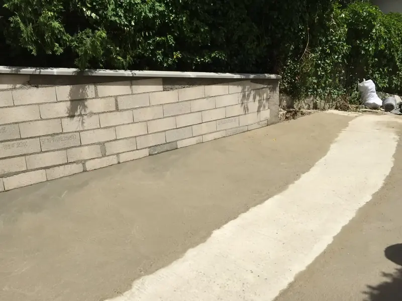 Dalle béton coulée au pied d'un mur de clôture enduit