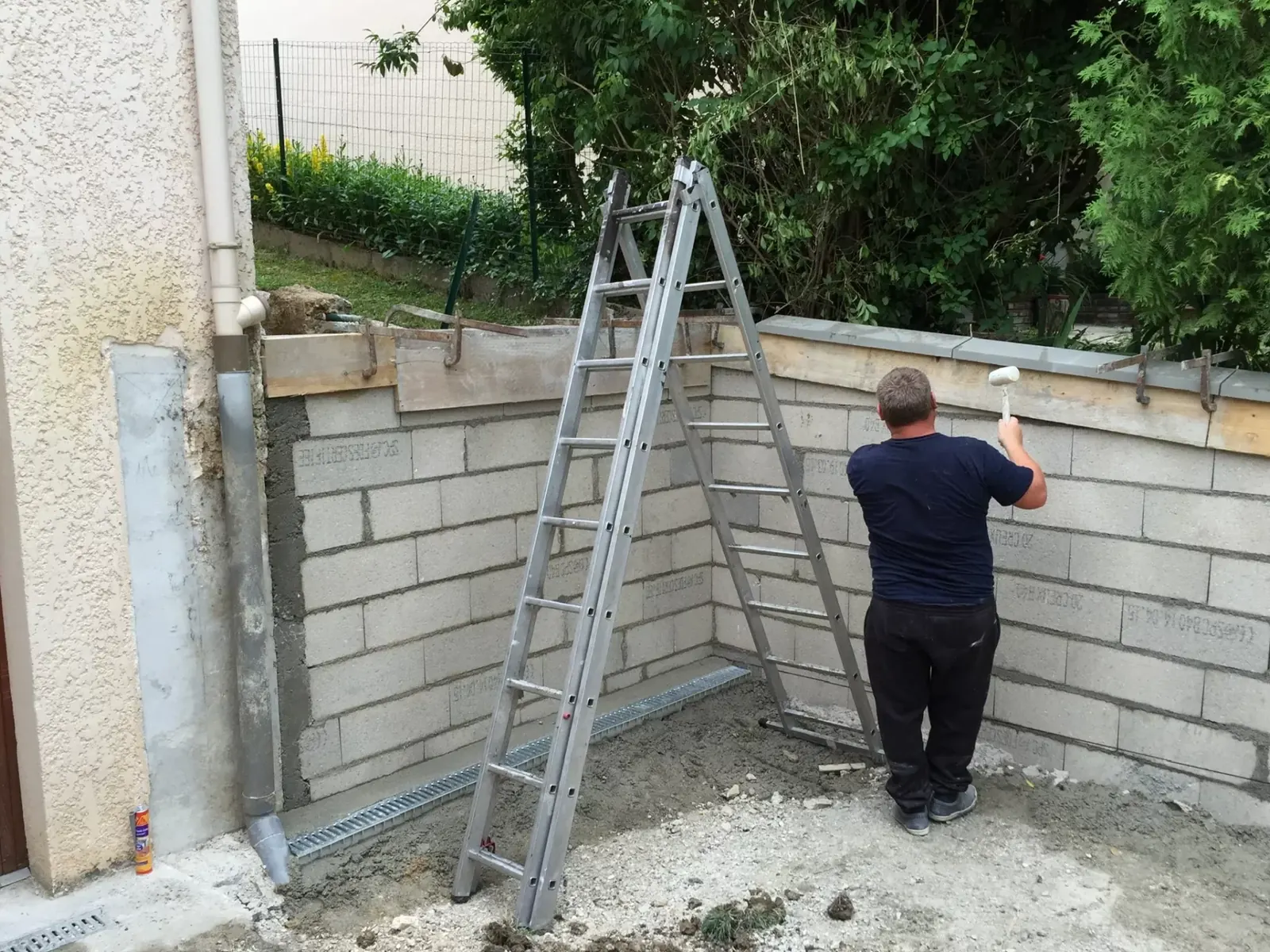Artisan maçon montant un mur en blocs béton dans un jardin