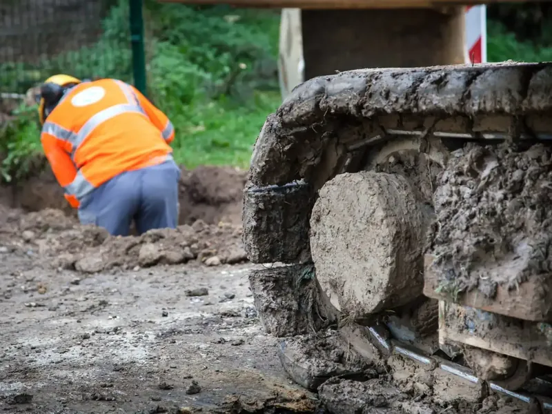 Ouvrier dans une tranchée de chantier, mini-pelle à côté